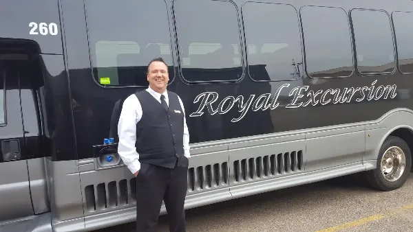 A professional driver standing in front of a Royal Excursion shuttle bus.