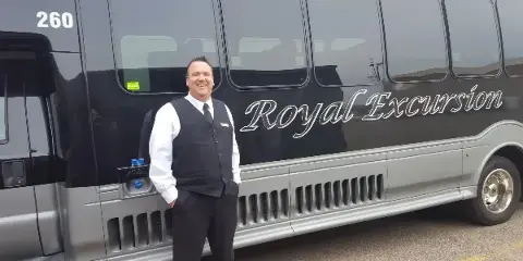 A professional driver standing in front of a Royal Excursion shuttle bus.