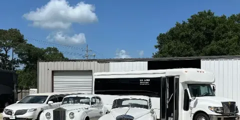 A white party bus and two white vintage wedding cars parked in front of a commercial building.