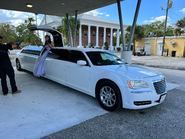 A white stretch limousine parked in a driveway with a passenger exiting the vehicle.