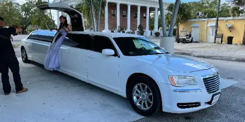 A white stretch limousine parked in a driveway with a passenger exiting the vehicle.