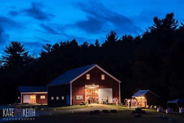 Exterior view of a red barn wedding venue at dusk with guests gathered outside.