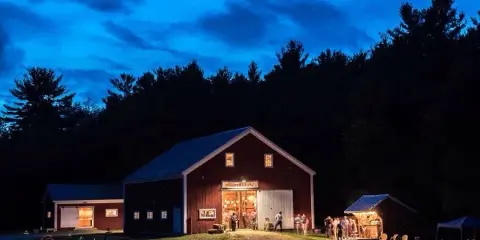 Exterior view of a red barn wedding venue at dusk with guests gathered outside.