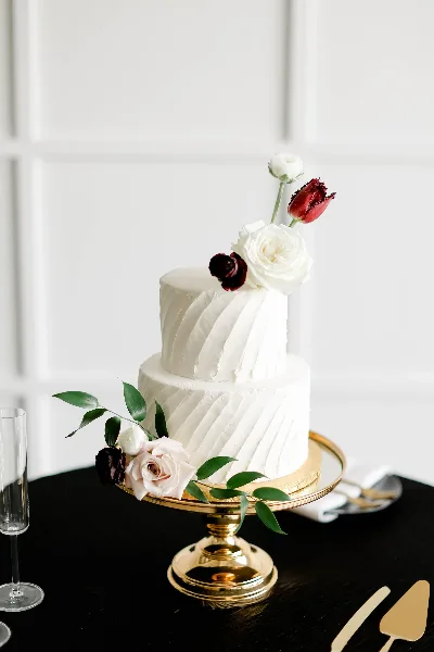 A two-tier white wedding cake decorated with fresh flowers on a gold stand.