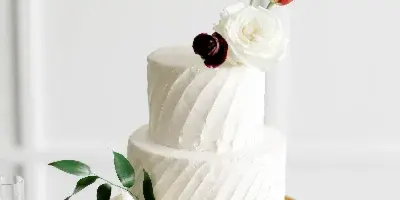 A two-tier white wedding cake decorated with fresh flowers on a gold stand.