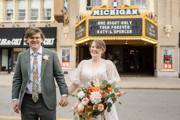 A bride and groom holding hands in front of the Michigan Theater marquee, which displays their names and the text 'One Night Only Then Forever'.