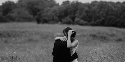 A black and white photograph of a bride and groom embracing in a grassy field.