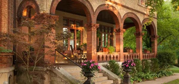 Exterior view of the Vrooman Mansion featuring arched columns, stone steps, and potted flowers.