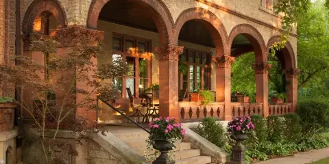 Exterior view of the Vrooman Mansion featuring arched columns, stone steps, and potted flowers.