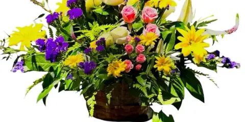 A colorful floral arrangement featuring yellow daisies, pink roses, and purple flowers in a woven basket.