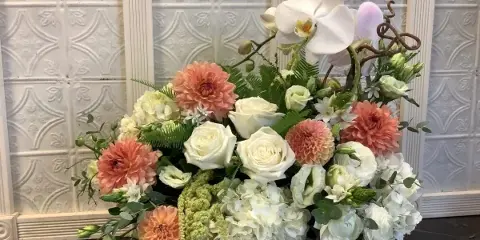 A custom floral arrangement featuring white roses, peach dahlias, and white orchids in a grey ceramic vessel.
