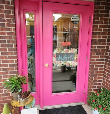 Pink storefront doors of Jayla's Flowers with potted plants and flowers displayed outside the entrance.