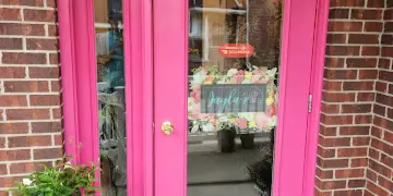 Pink storefront doors of Jayla's Flowers with potted plants and flowers displayed outside the entrance.