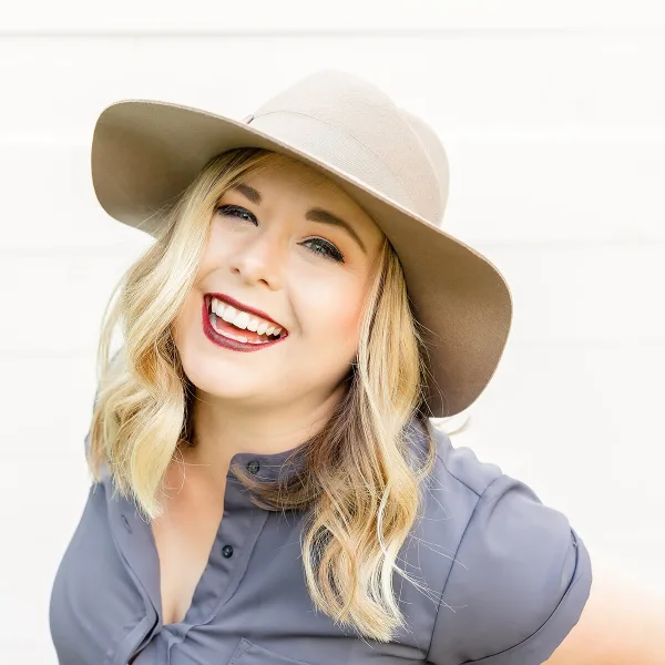 Portrait of a smiling blonde woman wearing a beige hat and a grey shirt.