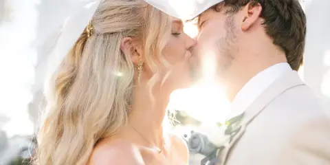 A bride and groom sharing a kiss under a white canopy with bright sunlight in the background.