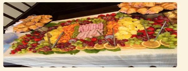 A catering table featuring a large, colorful platter of assorted fruits, sliced meats, and pastries.