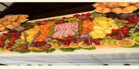 A catering table featuring a large, colorful platter of assorted fruits, sliced meats, and pastries.