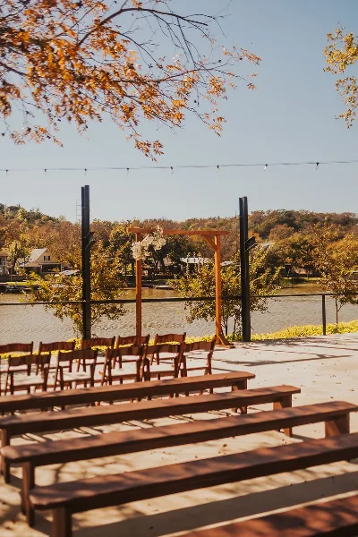 A wooden wedding arch and rows of wooden chairs set up outdoors near a body of water.