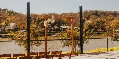 A wooden wedding arch and rows of wooden chairs set up outdoors near a body of water.