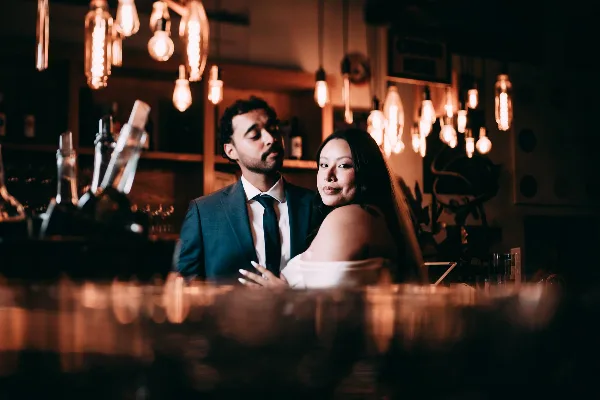 Cinematic portrait of a wedding couple in a dimly lit bar with Edison lights.