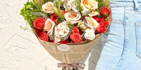 A hand-tied bouquet of red and peach roses wrapped in newspaper-style paper with a Fliorens ribbon.
