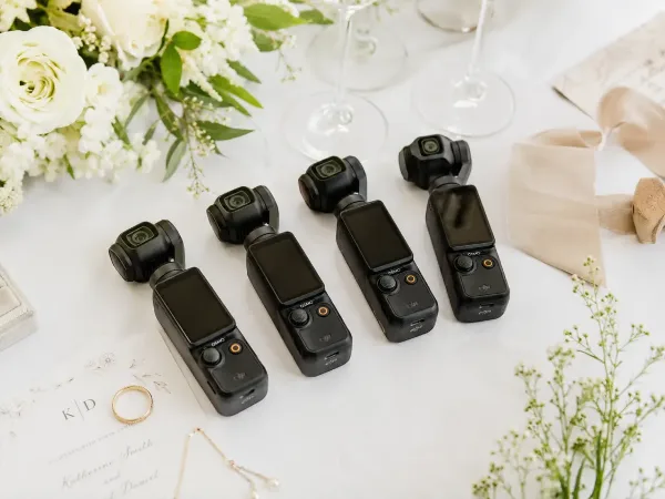 Four pocket cameras laid out on a white wedding table beside the flowers, the invitation and the rings