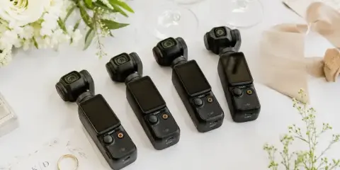 Four pocket cameras laid out on a white wedding table beside the flowers, the invitation and the rings