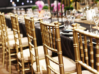 Rows of gold chiavari chairs set up at a dining table with tableware and glassware.