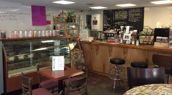 Interior view of a coffee shop showing a wooden counter, espresso machine, pastry display case, and menu board.
