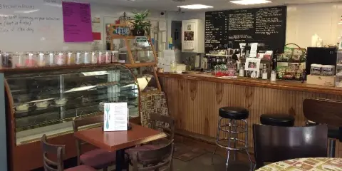Interior view of a coffee shop showing a wooden counter, espresso machine, pastry display case, and menu board.