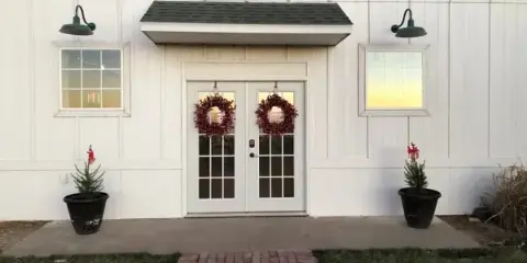 Exterior view of a white barn venue with double glass doors, brick walkway, and holiday wreaths.