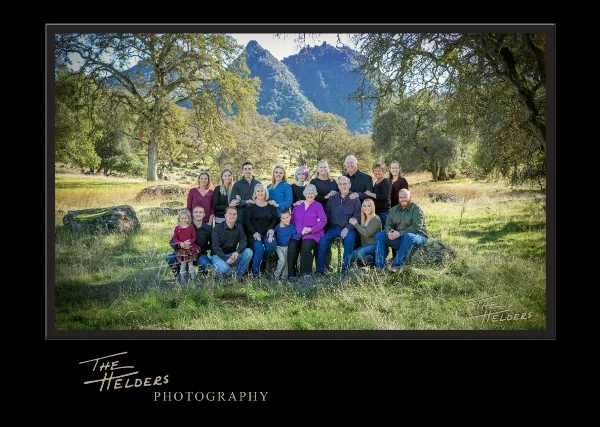 A professional outdoor family portrait featuring multiple generations of a family posing in a grassy field with mountains in the background.