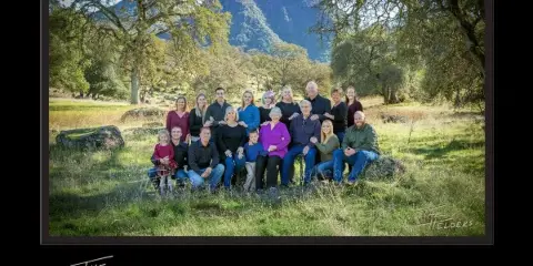 A professional outdoor family portrait featuring multiple generations of a family posing in a grassy field with mountains in the background.