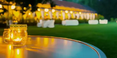 An outdoor event setup featuring a large white tent, white chair covers, and a table with lit candles in the foreground.