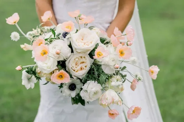 A bride holding a large, cascading wedding bouquet of white and peach flowers.