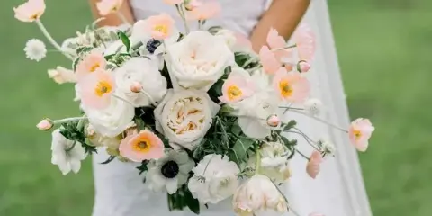 A bride holding a large, cascading wedding bouquet of white and peach flowers.