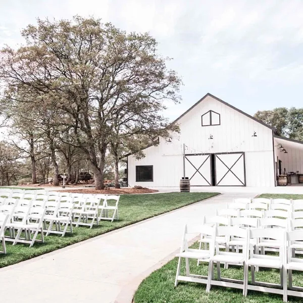 Exterior view of a white barn wedding venue with rows of white ceremony chairs set up on the lawn.