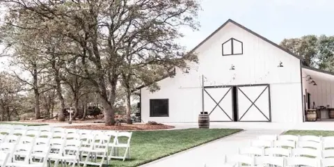 Exterior view of a white barn wedding venue with rows of white ceremony chairs set up on the lawn.