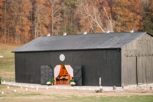 Exterior view of a black wooden barn wedding venue with a decorated entrance and surrounding grassy field.