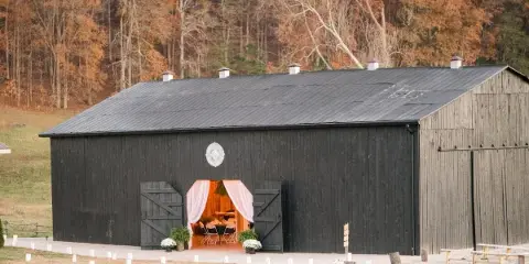 Exterior view of a black wooden barn wedding venue with a decorated entrance and surrounding grassy field.