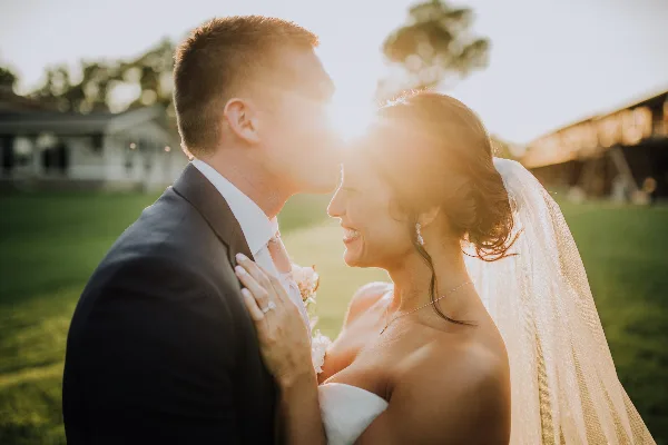 A bride and groom sharing a kiss outdoors in a field during golden hour.