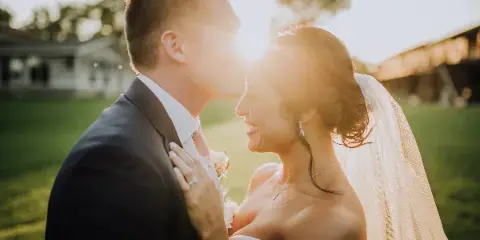 A bride and groom sharing a kiss outdoors in a field during golden hour.