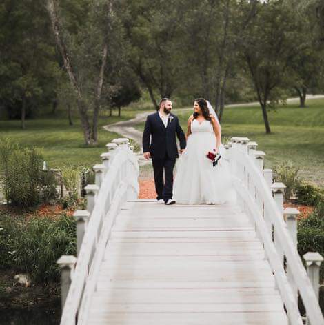 A bride and groom walking across a white wooden bridge at a wedding venue.