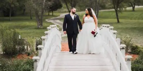 A bride and groom walking across a white wooden bridge at a wedding venue.