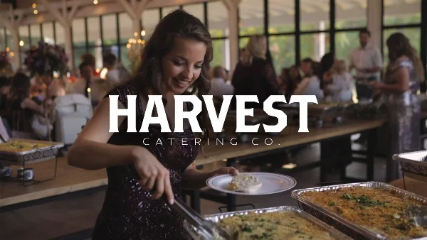 A woman serving herself food from a buffet line at a Harvest Catering event.