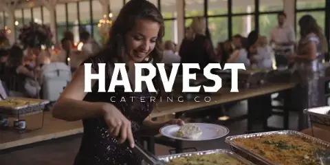 A woman serving herself food from a buffet line at a Harvest Catering event.