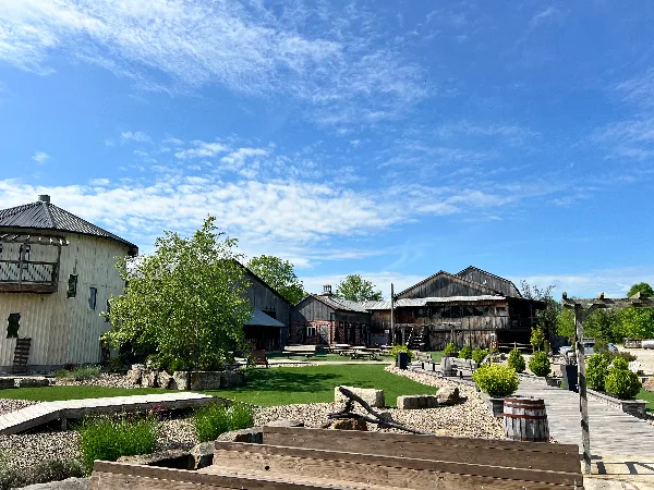 Exterior view of a rustic barn venue with a grassy lawn and wooden seating under a blue sky.