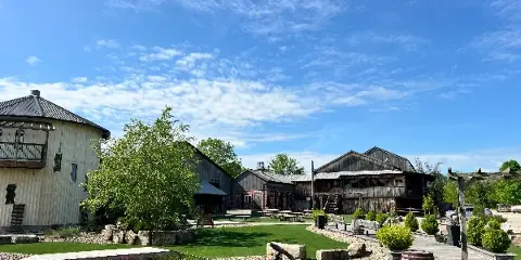 Exterior view of a rustic barn venue with a grassy lawn and wooden seating under a blue sky.