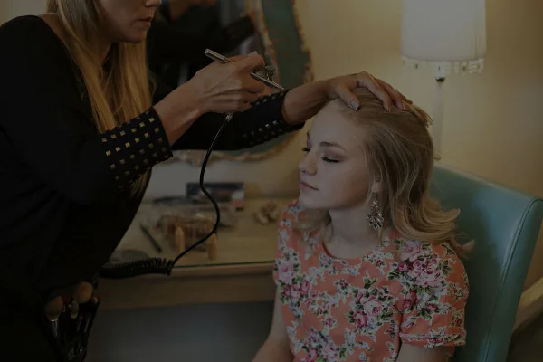 A makeup artist applying airbrush makeup to a seated client.