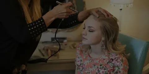A makeup artist applying airbrush makeup to a seated client.